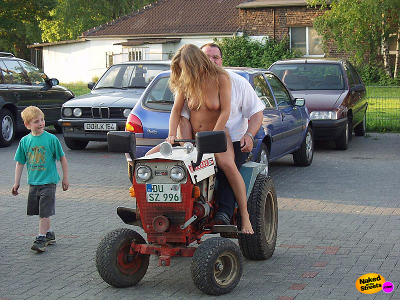 Blonde girl rides a tractor in the nude with a kid watching