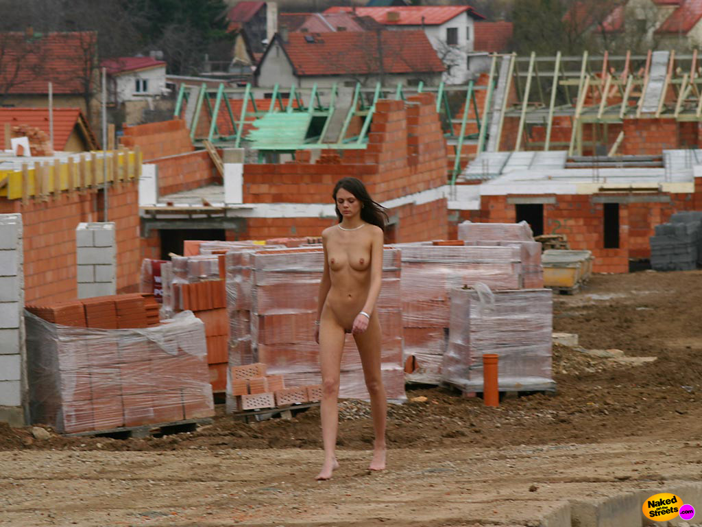 Slim brunette teen walks along a construction site with nothing on