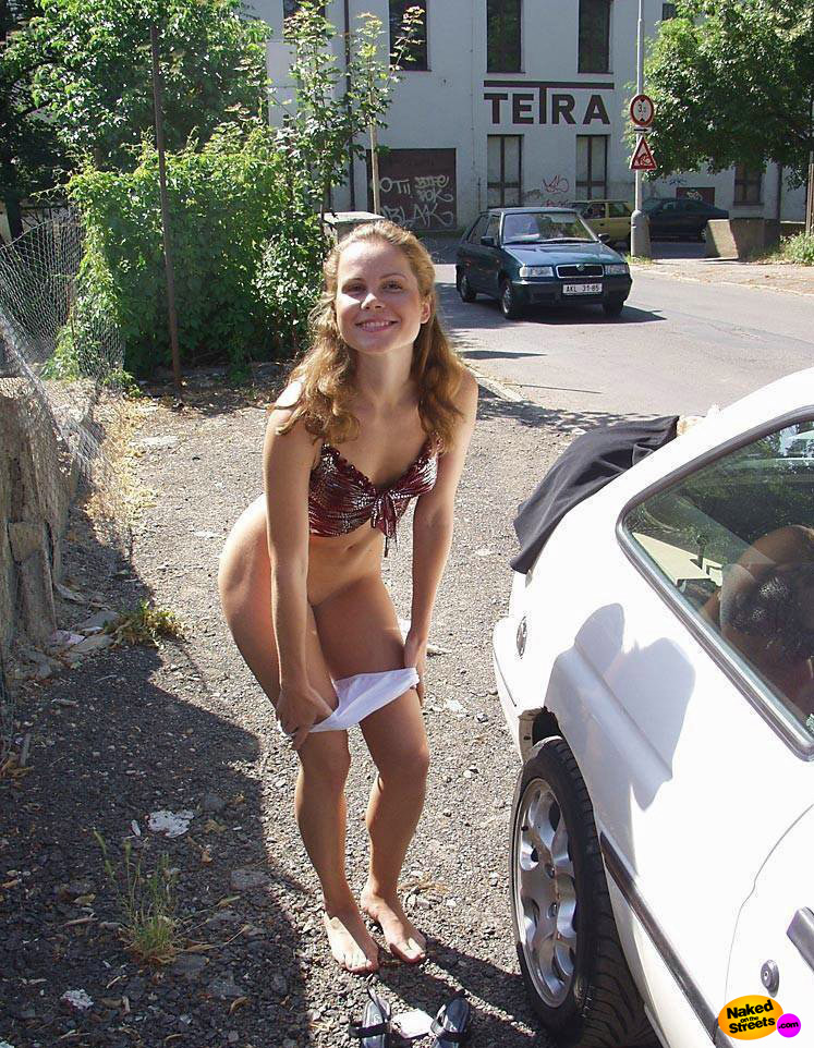 Teen girl undresses in public next to a car