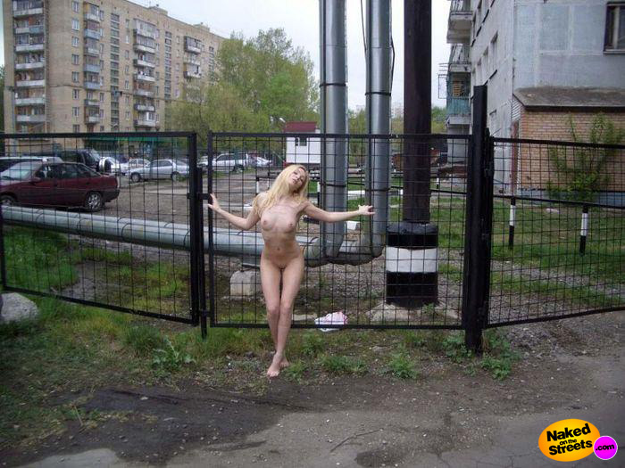 Kinky teen slut posing fully nude against a fence in a bad part of town