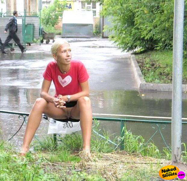 Short haired blonde hoochie sits on a fence, flashing her pussy under her skirt