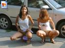 Gorgeous girls show off their snatches on the street behind a car