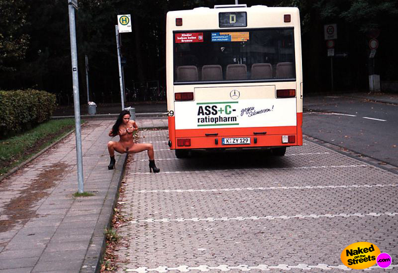 Hot nude brunette posing next to a bus with spread legs