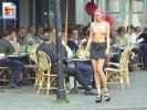Slender topless chick with pink hair walking by a crowded terrace